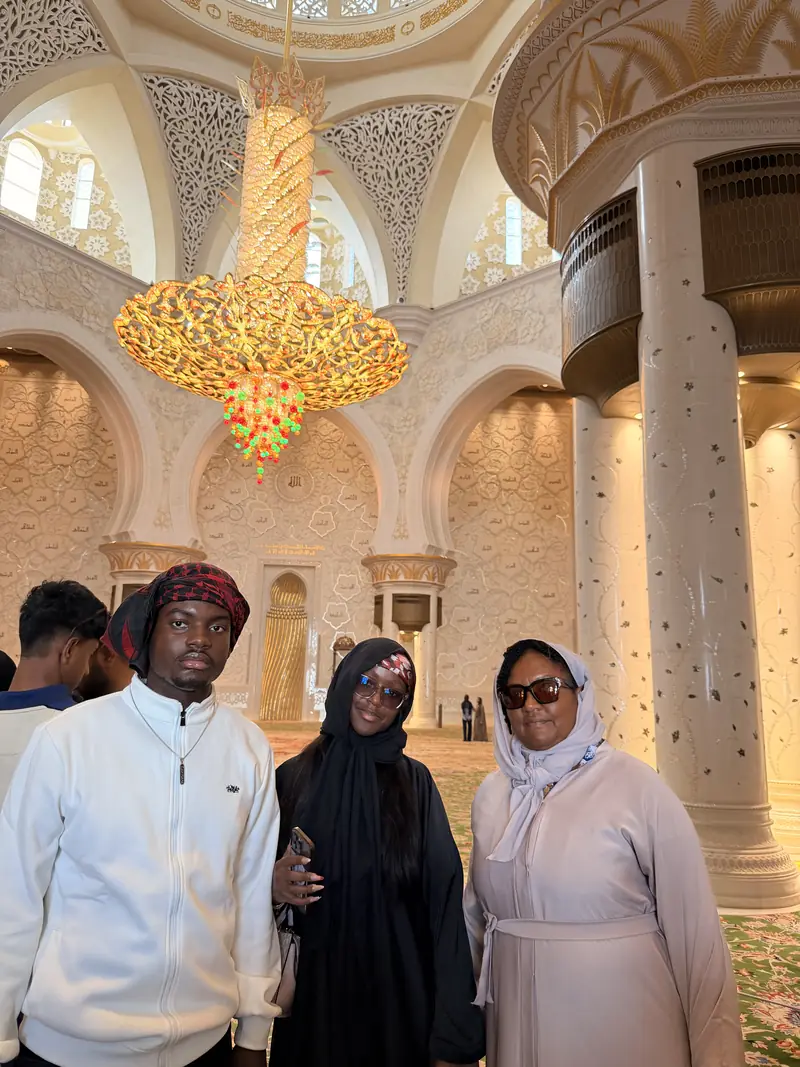 Three travellers inside the Grand Mosque beneath a large gold chandelier