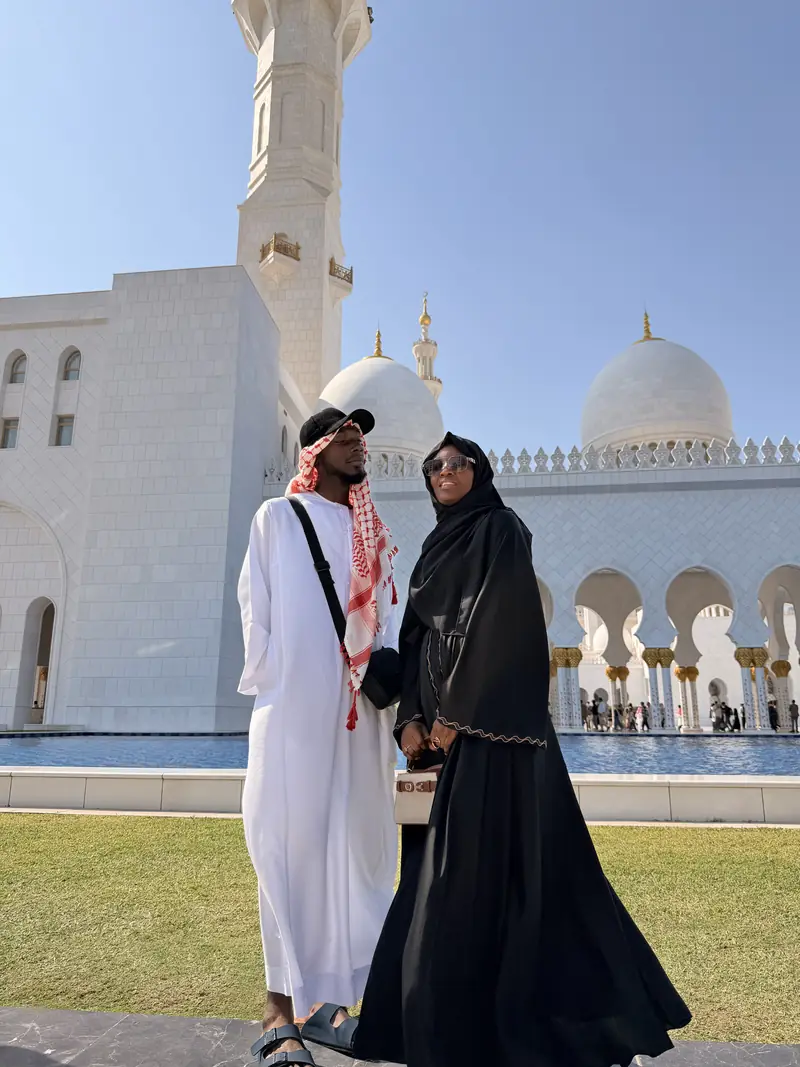 A couple in a white kandura and black abaya in front of the Sheikh Zayed Grand Mosque