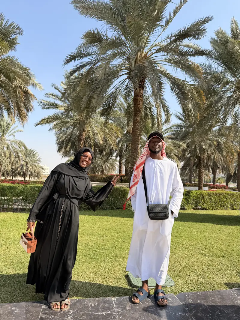 A couple in traditional dress standing under palm trees at the Sheikh Zayed Grand Mosque