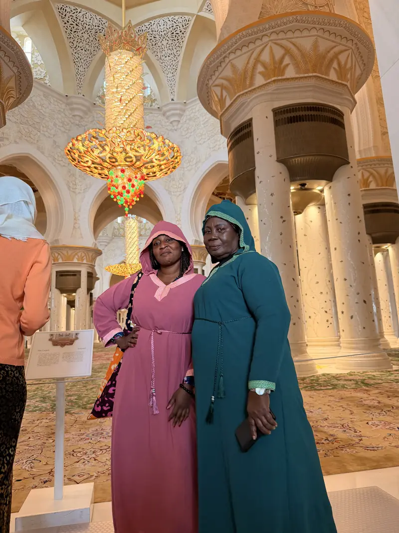 Two women in abayas inside the ornate prayer hall of the Sheikh Zayed Grand Mosque