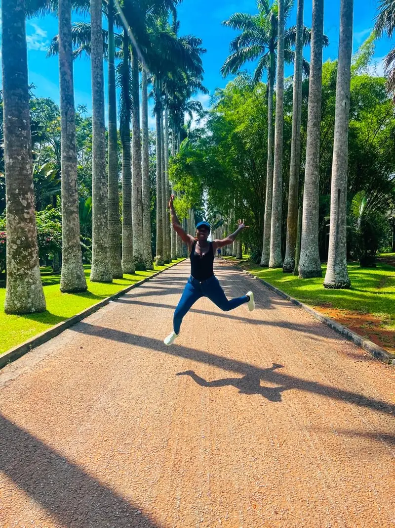A traveller jumping mid-air on a road lined with tall palm trees at Aburi Botanical Gardens