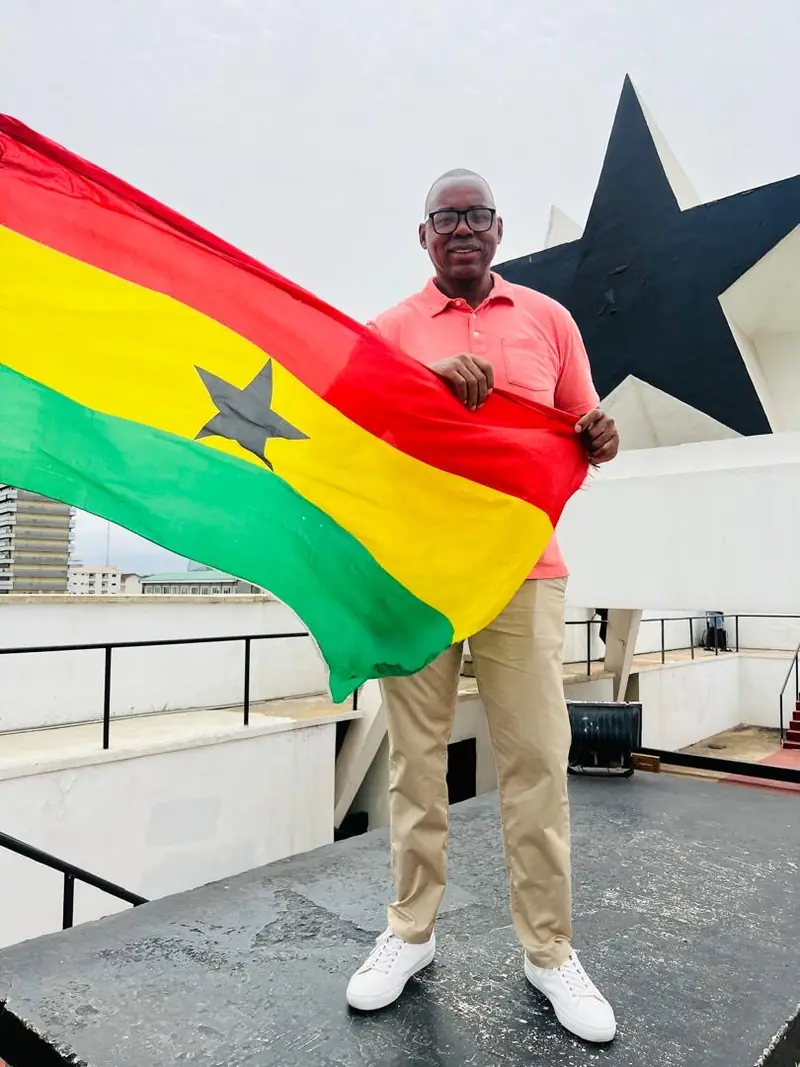 A traveller holding a Ghana flag beside the Black Star monument in Accra