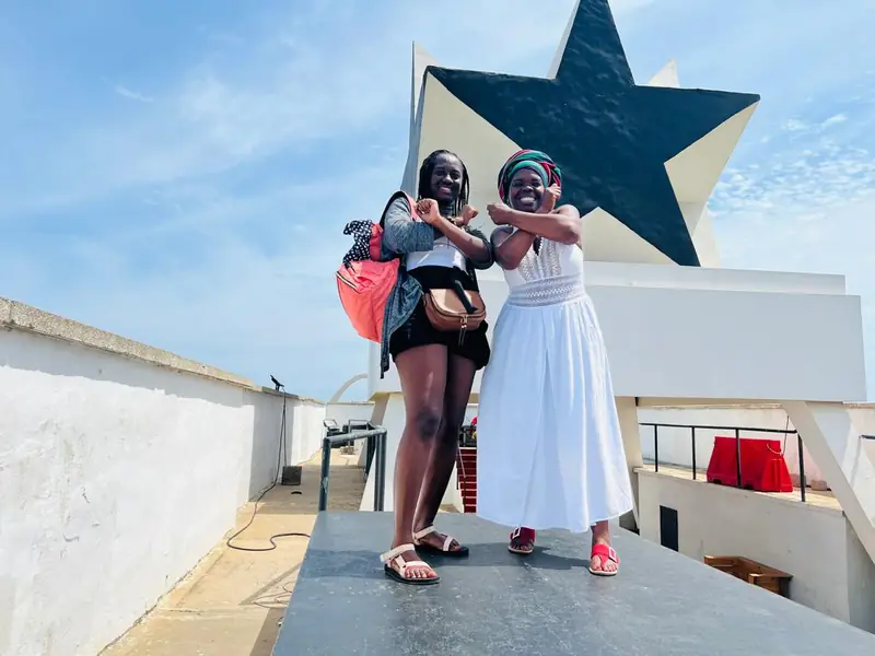 Two friends posing under the Black Star monument at Black Star Square
