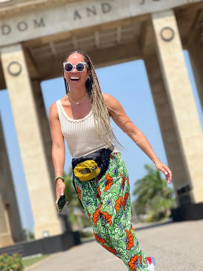 A traveller in sunglasses and African print trousers dancing beneath Independence Arch