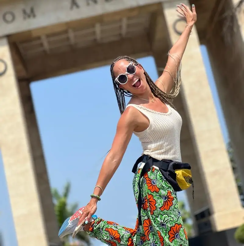 A smiling traveller in African print trousers leaping beneath Independence Arch