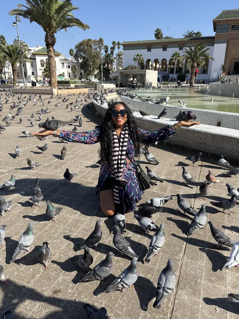A traveller crouching with open arms among pigeons at Mohammed V Square