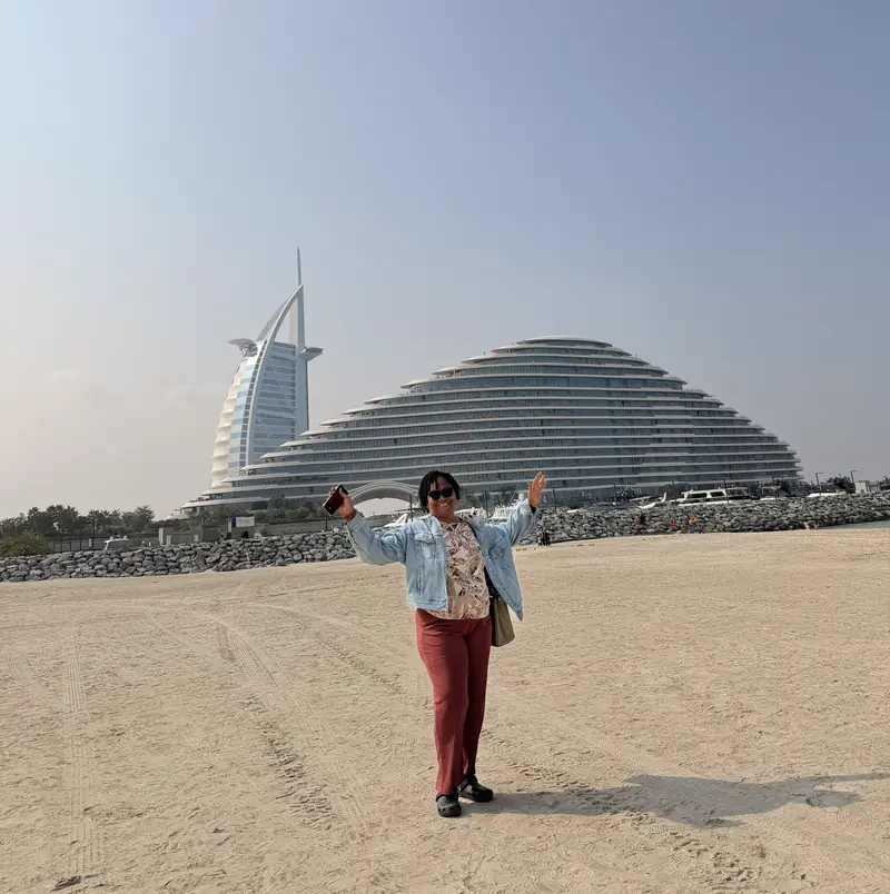 A traveller waving on the beach with the Burj Al Arab and a curved hotel behind her