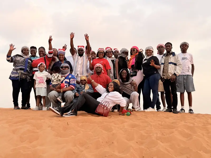 A large Myma Travels group in Santa hats cheering on a sand dune in the Dubai desert
