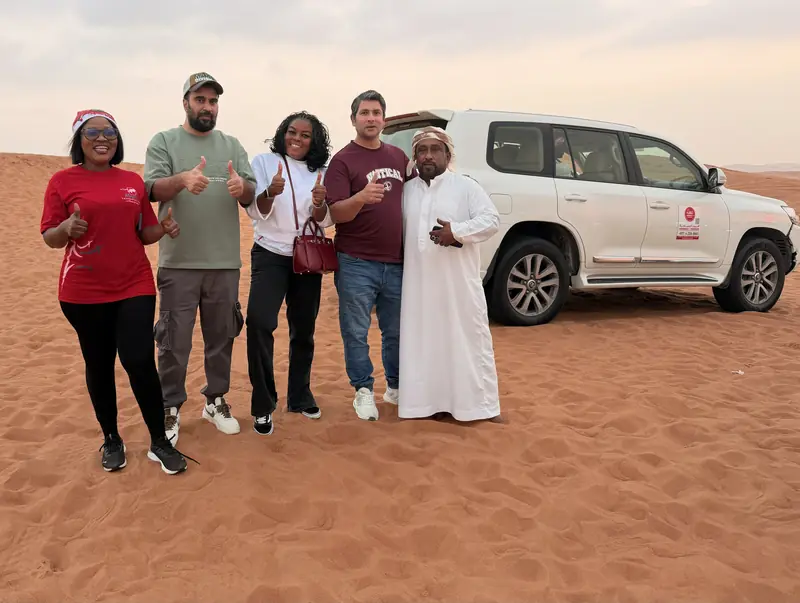 Four travellers with their Emirati safari guide beside a white 4x4 in the desert