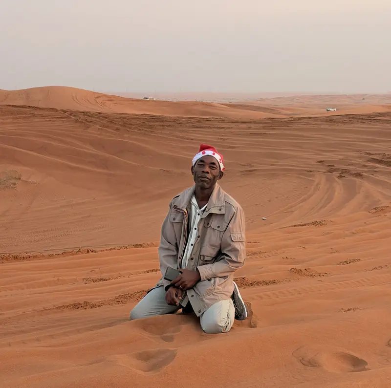 A traveller in a Santa hat kneeling on red sand dunes in the Dubai desert