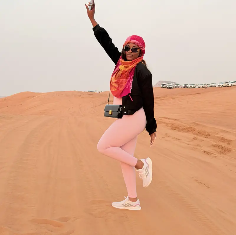 A traveller in a pink headscarf striking a pose on the sand dunes outside Dubai