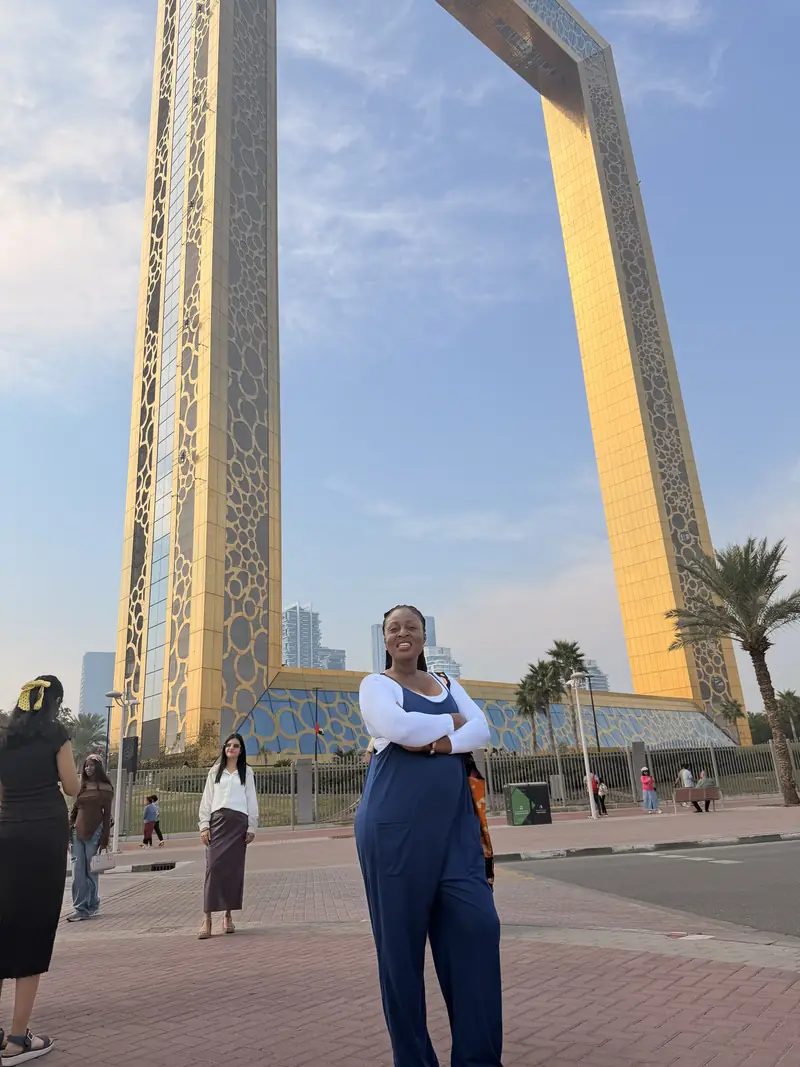A traveller in denim dungarees standing in front of the golden Dubai Frame