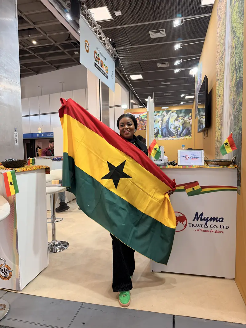 A Myma Travels team member holding a Ghana flag at the Myma Travels stand