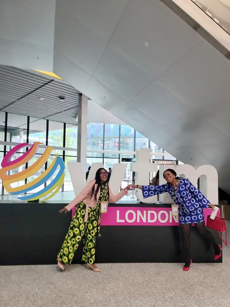Two members of the Myma Travels team posing by the WTM London sign