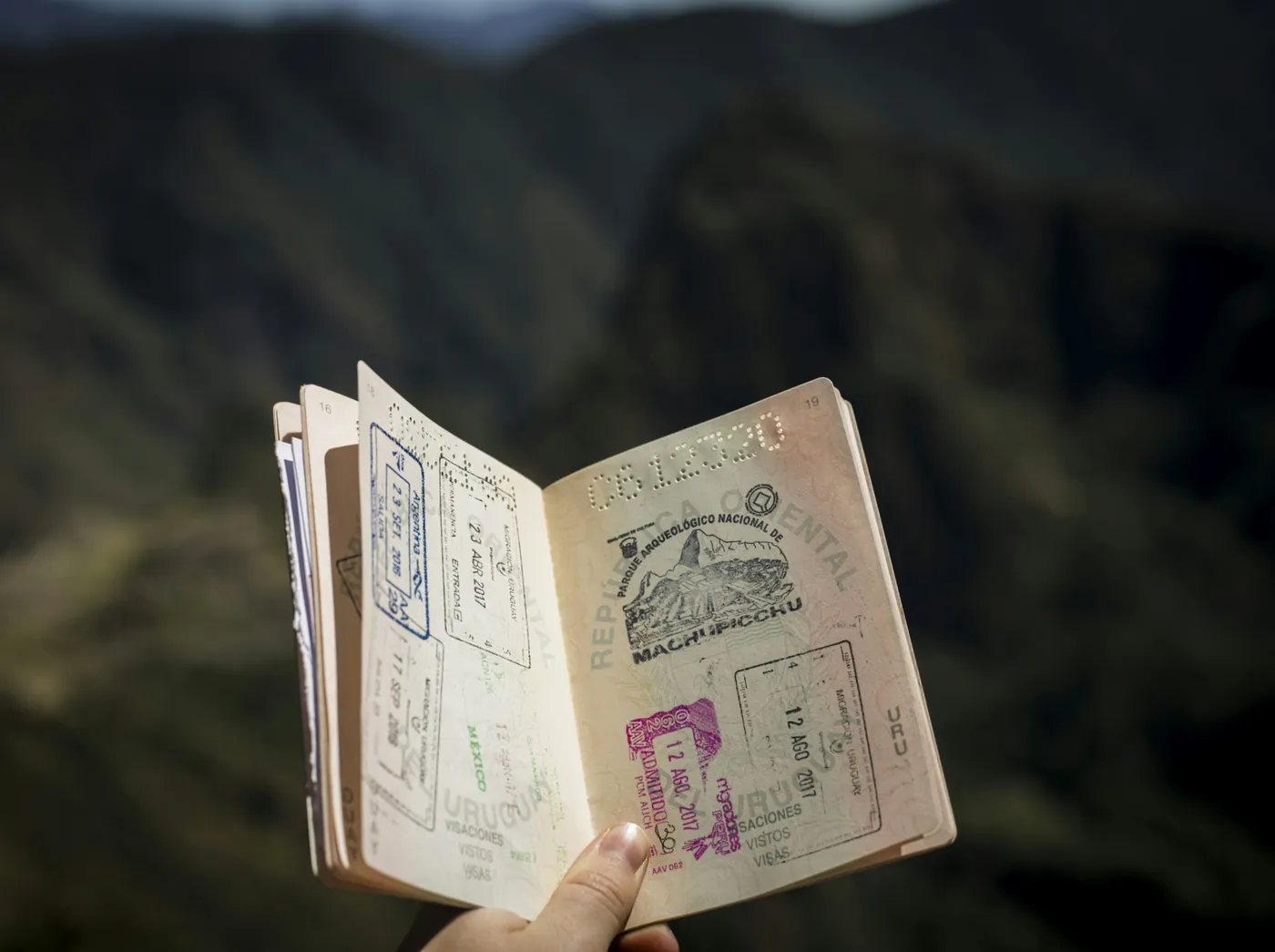 A hand holding open a passport filled with entry stamps and visas